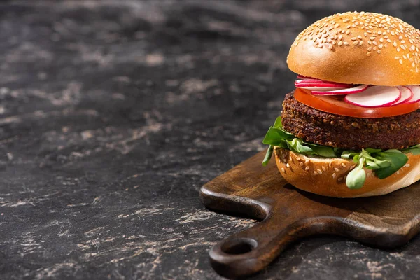 Tasty vegan burger with vegetables served on wooden cutting board on textured surface — Stock Photo