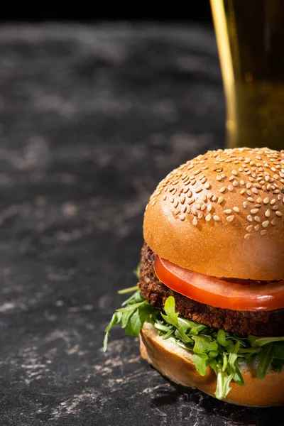 Enfoque selectivo de sabrosa hamburguesa vegana con tomate y verduras servidas en superficie texturizada con cerveza - foto de stock