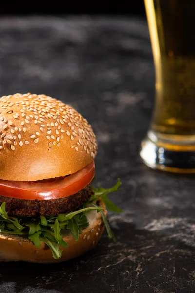 Selektiver Schwerpunkt des leckeren veganen Burgers mit Tomaten und Gemüse, serviert auf strukturierter Oberfläche mit Bier — Stockfoto