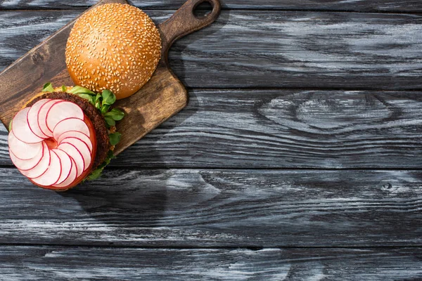 Top view of tasty vegan burger with microgreens, radish, tomato on cutting board served on wooden table — Stock Photo