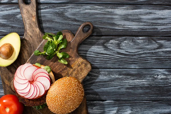Top view of tasty vegan burger with microgreens, radish, tomato and avocado on cutting boards served on wooden table — Stock Photo