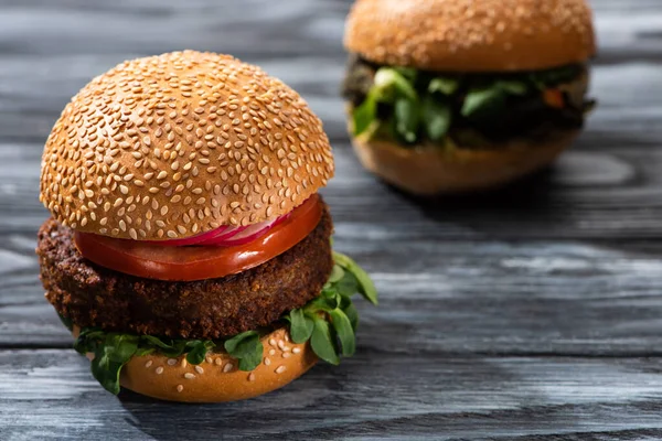 Selective focus of tasty vegan burgers with vegetables served on wooden table — Stock Photo
