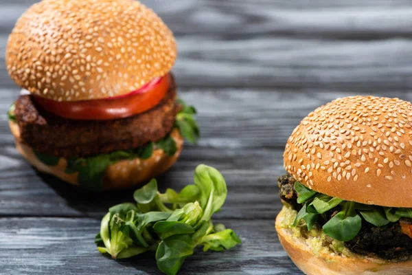 Enfoque selectivo de sabrosas hamburguesas veganas con verduras servidas en mesa de madera - foto de stock