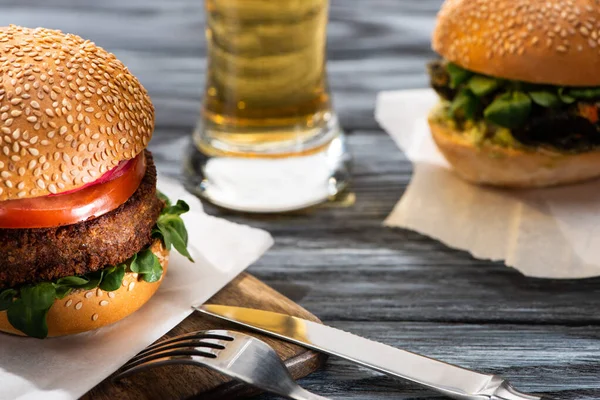 Selective focus of tasty vegan burgers served on wooden table with beer and cutlery — Stock Photo