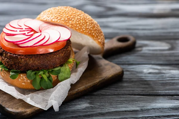 Leckerer veganer Burger auf Schneidebrett auf Holztisch serviert — Stockfoto