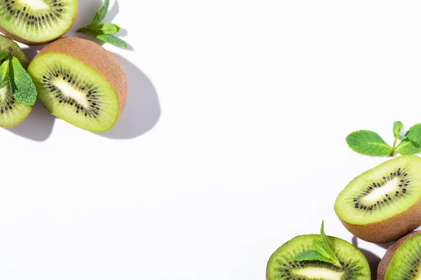 Vue de dessus des moitiés de kiwis mûrs près de menthe poivrée verte sur blanc — Photo de stock