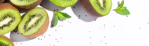 Panoramic orientation of ripe kiwi fruit halves near peppermint and black seeds on white — Stock Photo