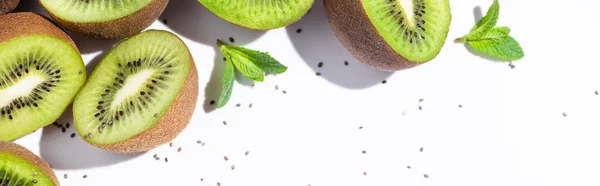 Orientation panoramique des moitiés de kiwis mûrs près de la menthe poivrée et des graines noires sur fond blanc — Photo de stock