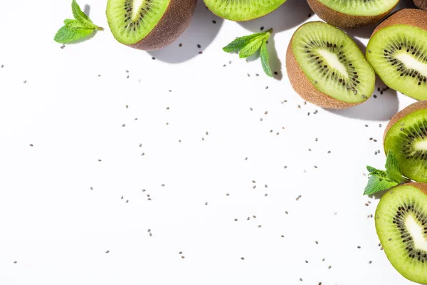 Blick von oben auf Bio-Kiwi-Fruchthälften in der Nähe von Pfefferminze und schwarzen Samen auf weißen — Stockfoto