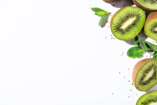 Top view of tasty kiwi fruit halves near green peppermint and black seeds on white — Stock Photo