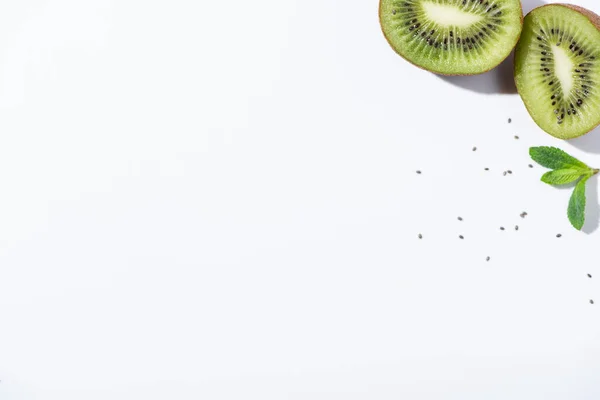 Top view of delicious kiwi fruit halves near green peppermint and black seeds on white — Stock Photo