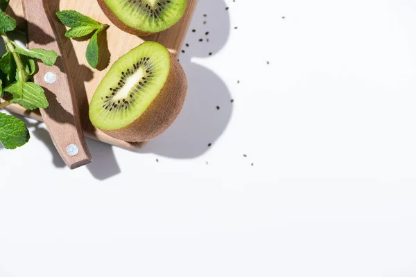 Vista superior de deliciosas metades de kiwi perto de hortelã-pimenta verde na tábua de corte em branco — Fotografia de Stock