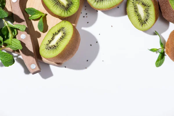 Vue de dessus de savoureux kiwis moitiés de fruits près de menthe poivrée verte sur planche à découper sur blanc — Photo de stock