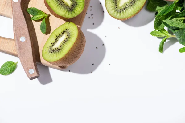 Вид на свежие фрукты киви рядом с зеленой мятой на разделочной доске на белом — стоковое фото