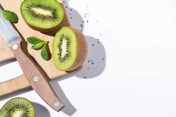 Vista superior de las frutas frescas de kiwi cerca de menta en la tabla de cortar en blanco - foto de stock