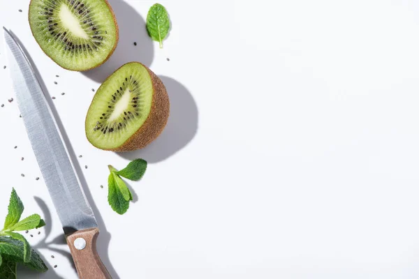 Vue de dessus des fruits kiwis savoureux près de menthe poivrée verte, couteau et graines noires sur blanc — Photo de stock