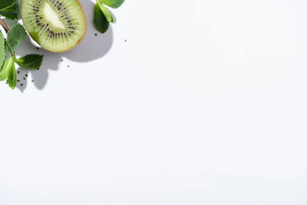 Вид зверху на зелену м'яту біля свіжих фруктів ківі та чорного насіння на білому — стокове фото
