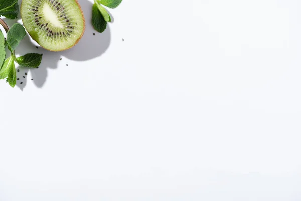 Top view of green peppermint near fresh kiwi fruit and black seeds on white — Stock Photo