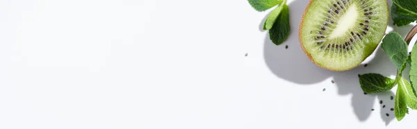 Horizontal crop of green peppermint near fresh kiwi fruit and black seeds on white — Stock Photo