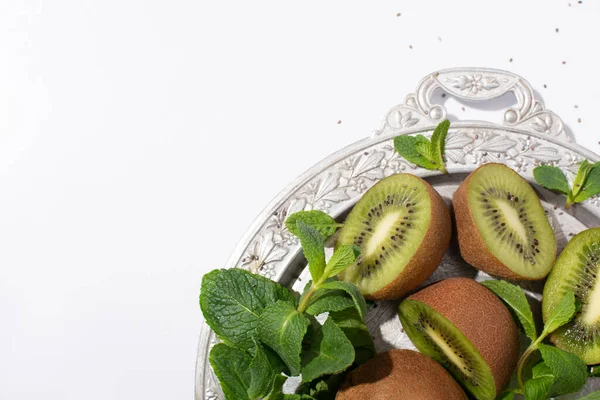 Top view of juicy kiwi fruits near fresh peppermint on silver plate isolated on white — Stock Photo