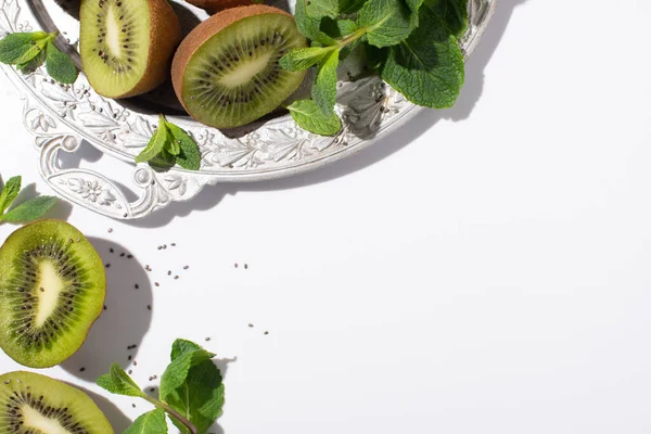 Vue de dessus des fruits verts de kiwi près de menthe poivrée fraîche sur la plaque d'argent sur blanc — Photo de stock