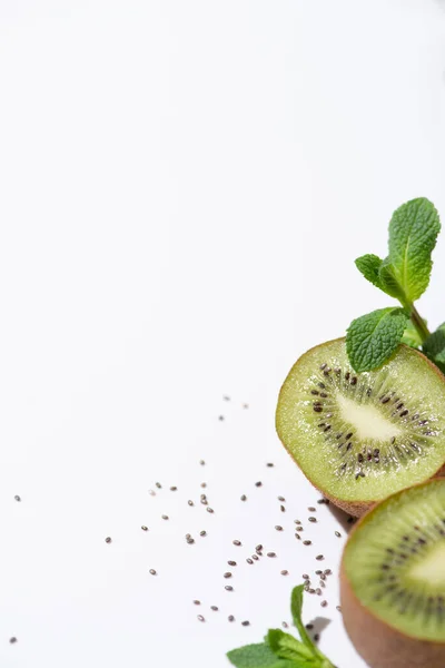 Fuoco selettivo di frutti di kiwi maturi vicino a menta piperita fresca e semi neri su bianco — Stock Photo