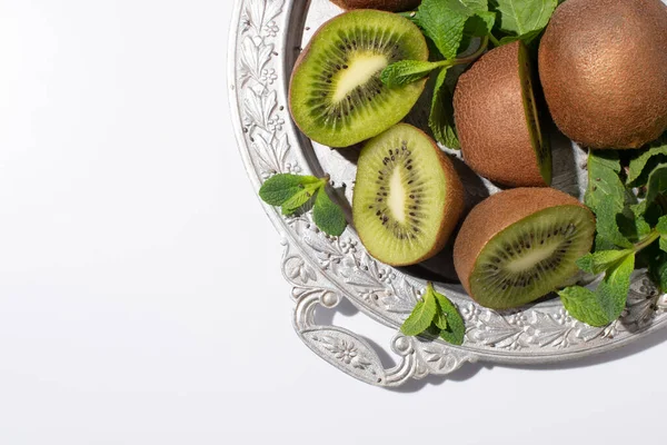 Вид на вкусные фрукты киви возле свежей мяты на серебряной тарелке, изолированной на белом — стоковое фото
