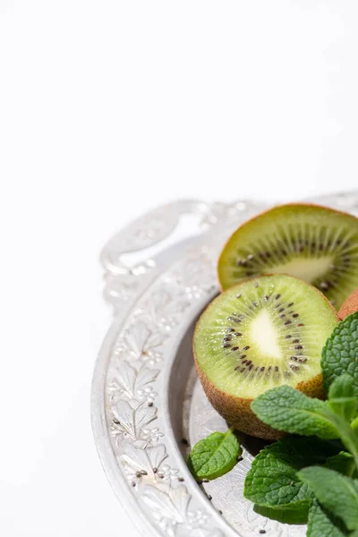 Selective focus of tasty kiwi fruits near fresh and green peppermint on silver plate isolated on white — Stock Photo