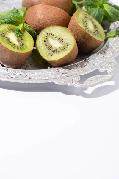 Вкусные фрукты киви возле свежей мяты на серебряной тарелке на белом — стоковое фото