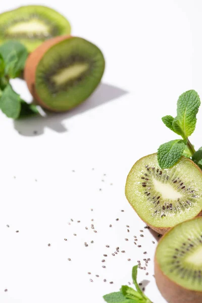 Messa a fuoco selettiva di gustosi kiwi vicino alla menta piperita fresca e semi neri su bianco — Foto stock