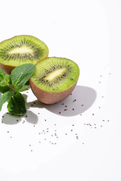 Sabrosas frutas kiwi cerca de menta fresca y semillas negras sobre blanco - foto de stock