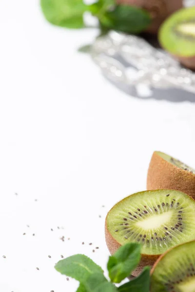 Fuoco selettivo di frutti di kiwi saporiti vicino a menta piperita e semi neri su bianco — Foto stock