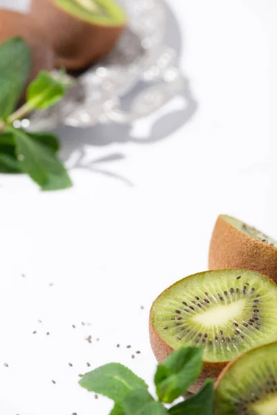 Selective focus of organic kiwi fruits near peppermint and black seeds on white — Stock Photo