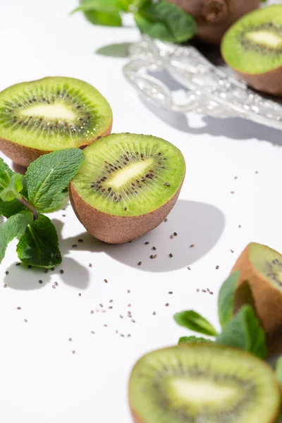 Selektiver Fokus von grünen Kiwi-Früchten in der Nähe von Pfefferminze und schwarzen Samen auf weißen — Stockfoto