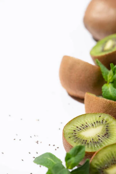 Selective focus of green kiwi fruits near organic peppermint and black seeds on white — Stock Photo