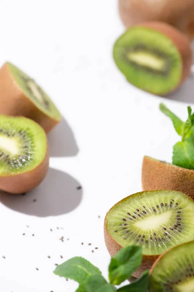 Selective focus of kiwi fruits near organic peppermint and black seeds on white — Stock Photo
