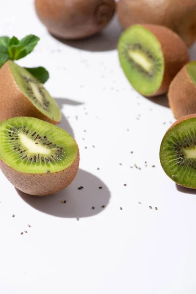 Selective focus of fresh kiwi fruits near organic peppermint and black seeds on white — Stock Photo