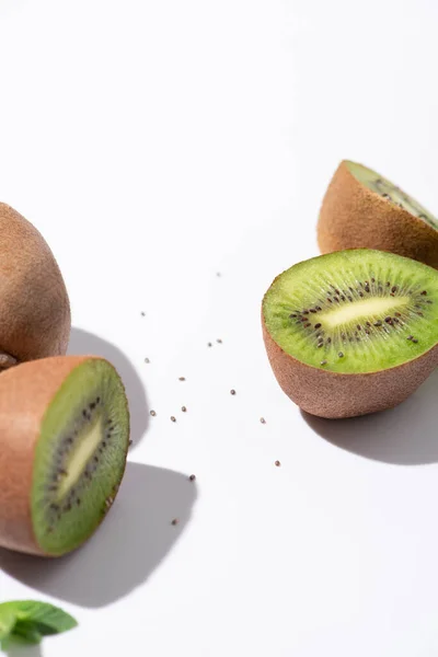 Selective focus of juicy kiwi fruits near green peppermint and black seeds on white — Stock Photo