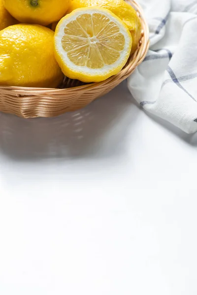 Close up view of basket of fresh lemons and napkin on white background — Stock Photo