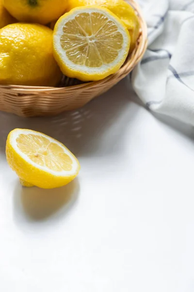 Close up view of basket of fresh lemons and napkin on white background — Stock Photo