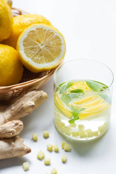 Close up view of fresh lemonade with mint in glass near basket of lemons and ginger root on white background — Stock Photo