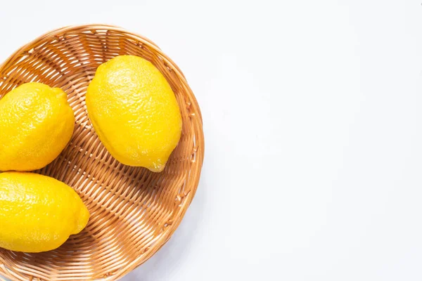 Верхний вид спелых лимонов в плетеной корзине на белом фоне — стоковое фото