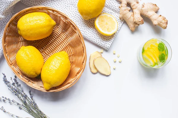 Vue de dessus de la limonade fraîche en verre près du panier de citrons, lavande et racine de gingembre sur fond blanc avec serviette — Photo de stock