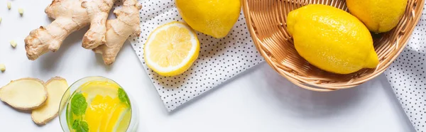 Vue du dessus de la limonade fraîche en verre près du panier de citrons et de racine de gingembre sur fond blanc avec serviette, image horizontale — Photo de stock