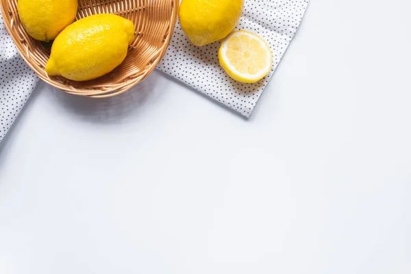 Top view of ripe lemons in wicker basket on white background with dotted napkin — Stock Photo