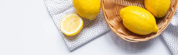 Верхний вид спелых лимонов в плетеной корзине на белом фоне с точечной салфеткой, горизонтальное изображение — стоковое фото