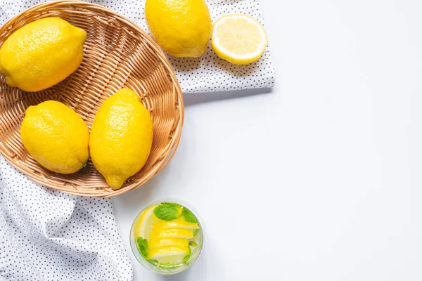 Top view of fresh lemonade in glass near basket of lemons on white background with napkin — Stock Photo