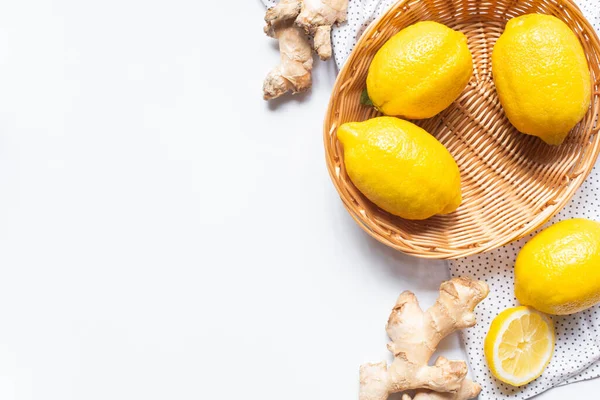 Draufsicht auf reife Zitronen im Weidenkorb auf weißem Hintergrund mit gepunkteter Serviette und Ingwerwurzel — Stockfoto