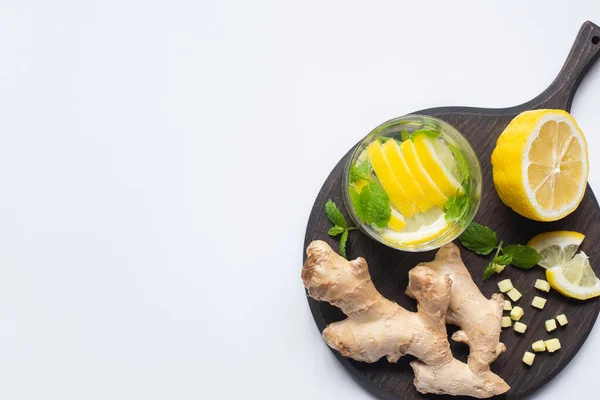 Top view of fresh lemonade in glass near lemons and ginger root on black wooden board on white background — Stock Photo