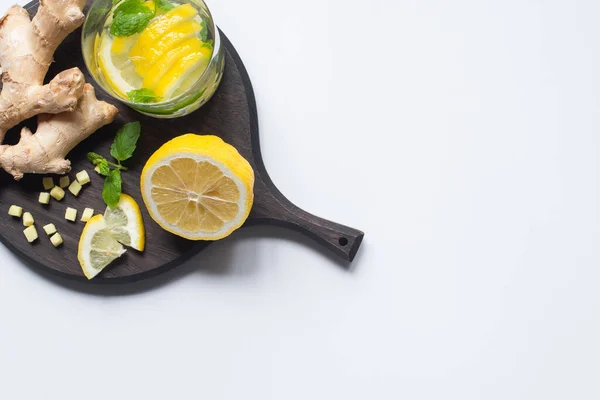 Vue de dessus de la limonade fraîche en verre près de citrons et racine de gingembre sur panneau en bois noir sur fond blanc — Photo de stock